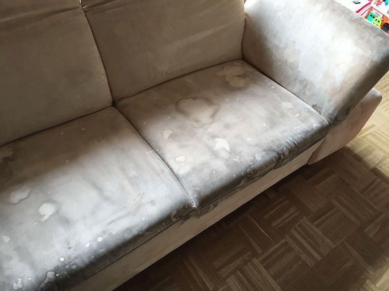 Schmutziges beiges Sofa mit Flecken und Verfärbungen in einem Raum mit Holzboden.