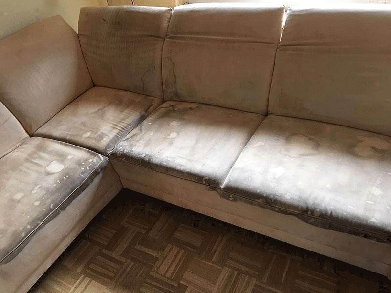 Schmutziges, abgenutztes beigefarbenes Sofa in einem Raum mit Holzboden.