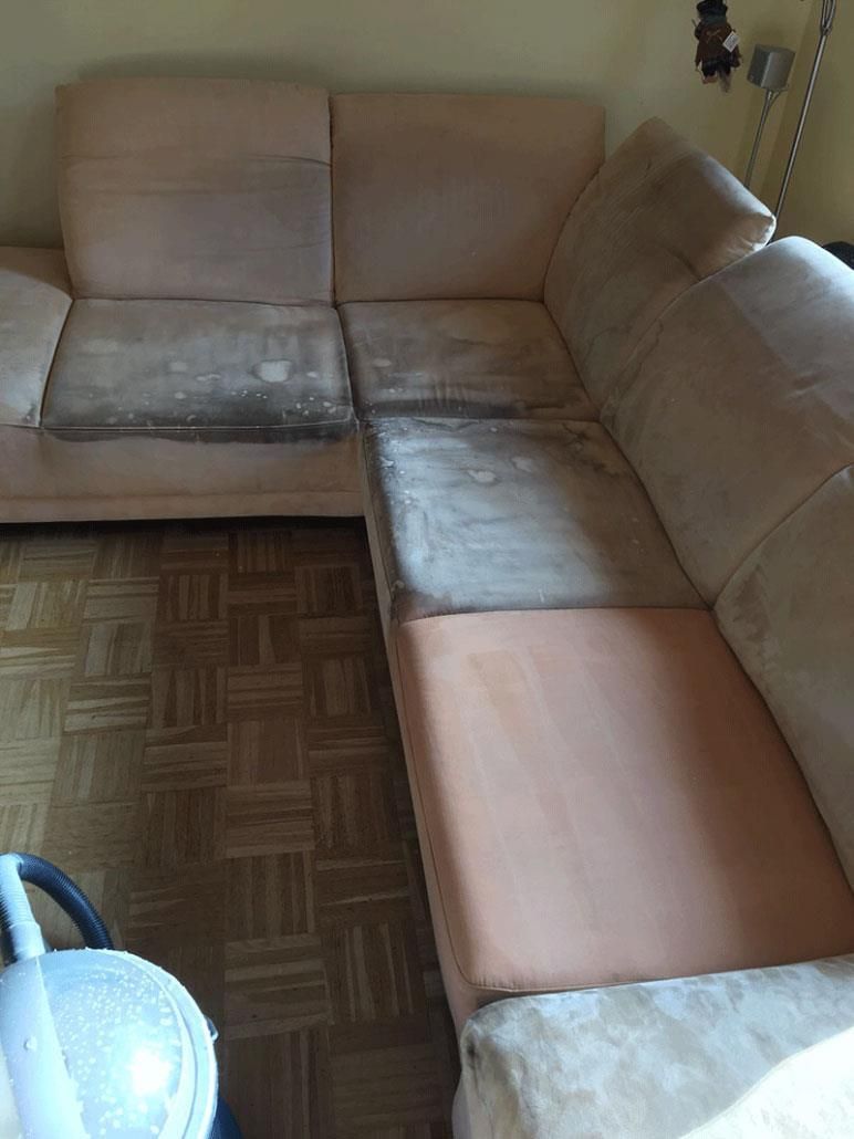 Ein schmutziges, beiges Sofa mit dunklen Flecken auf den Kissen in einem Raum mit Holzboden.