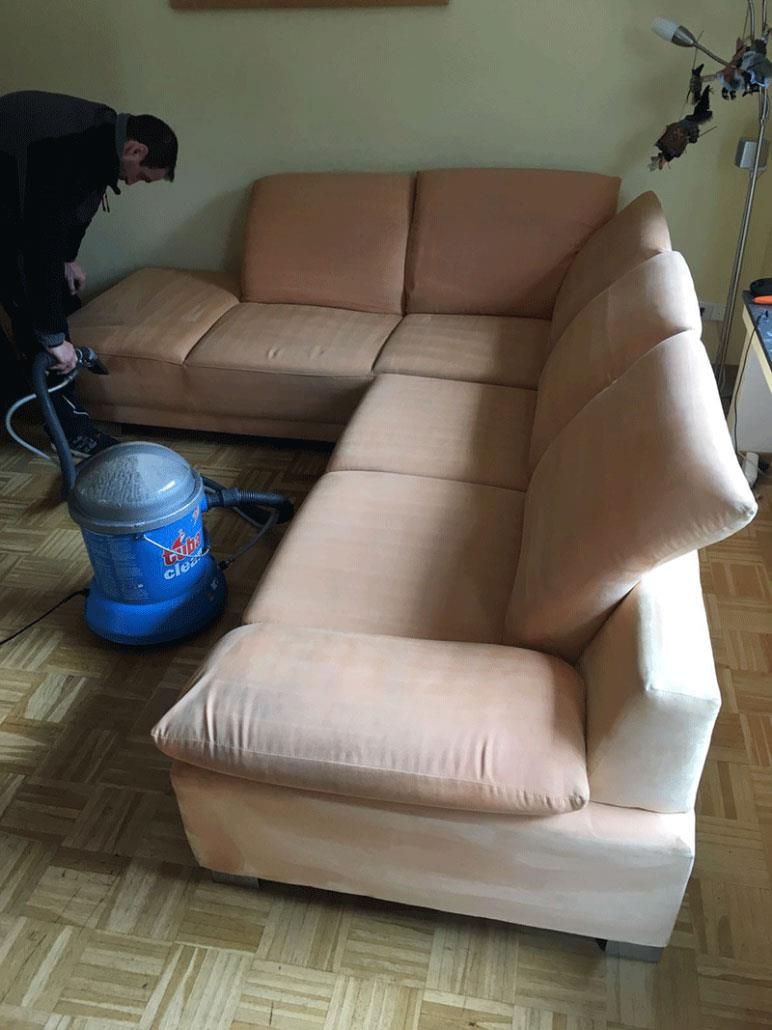 Person reinigt ein hellpfirsichfarbenes Sofa mit einem blauen Polsterreiniger.
