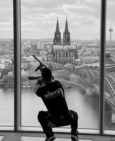 Fensterputzer vor einem großen Fenster, beim Putzen, im Hintergrund ist der Kölner Dom zu sehen.