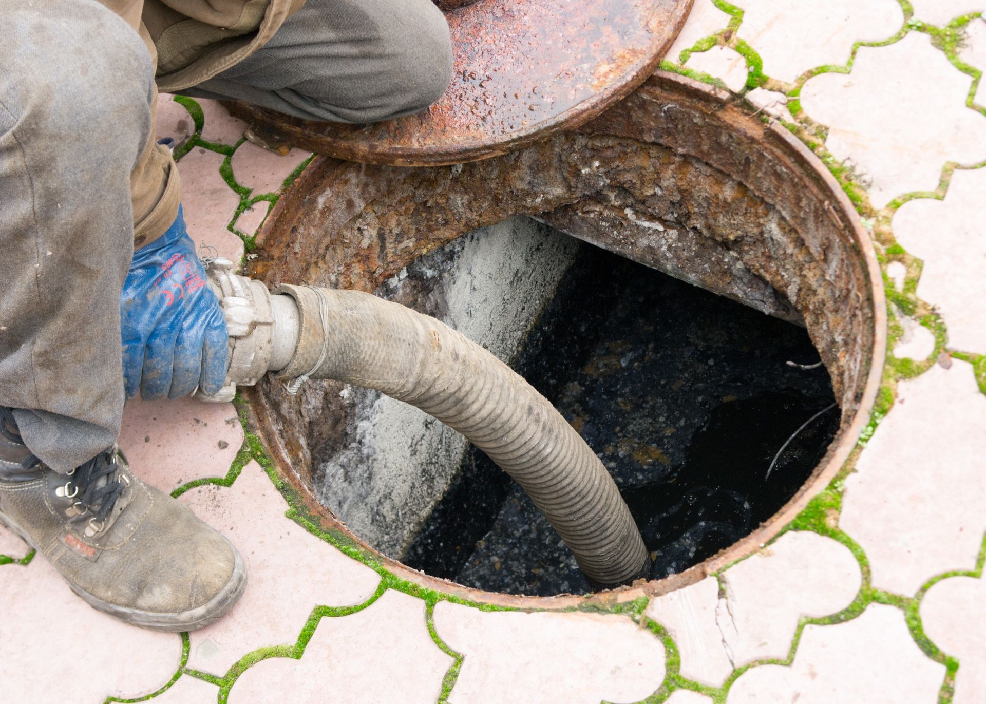 Un hombre está bombeando agua a una tapa de alcantarilla con una manguera.