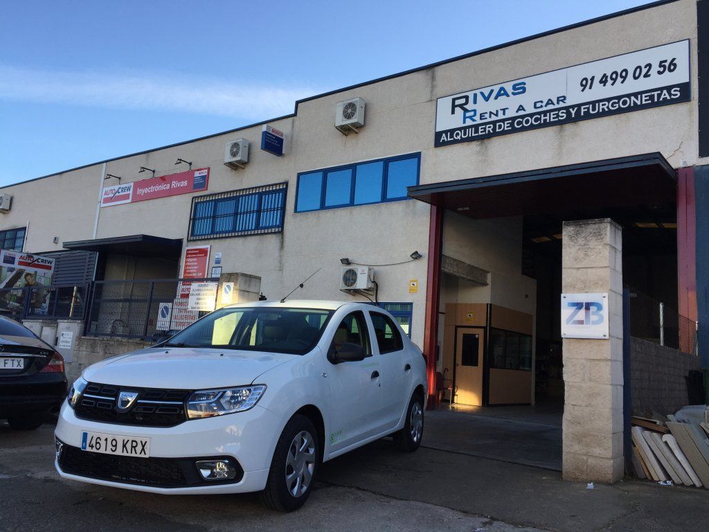Un coche blanco está estacionado frente a un edificio que dice Rivas.