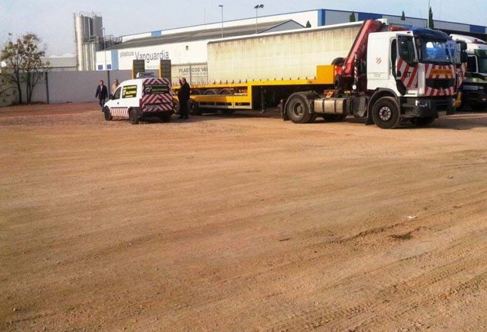 Un camión con una grúa en la parte trasera está estacionado en un terreno de tierra.