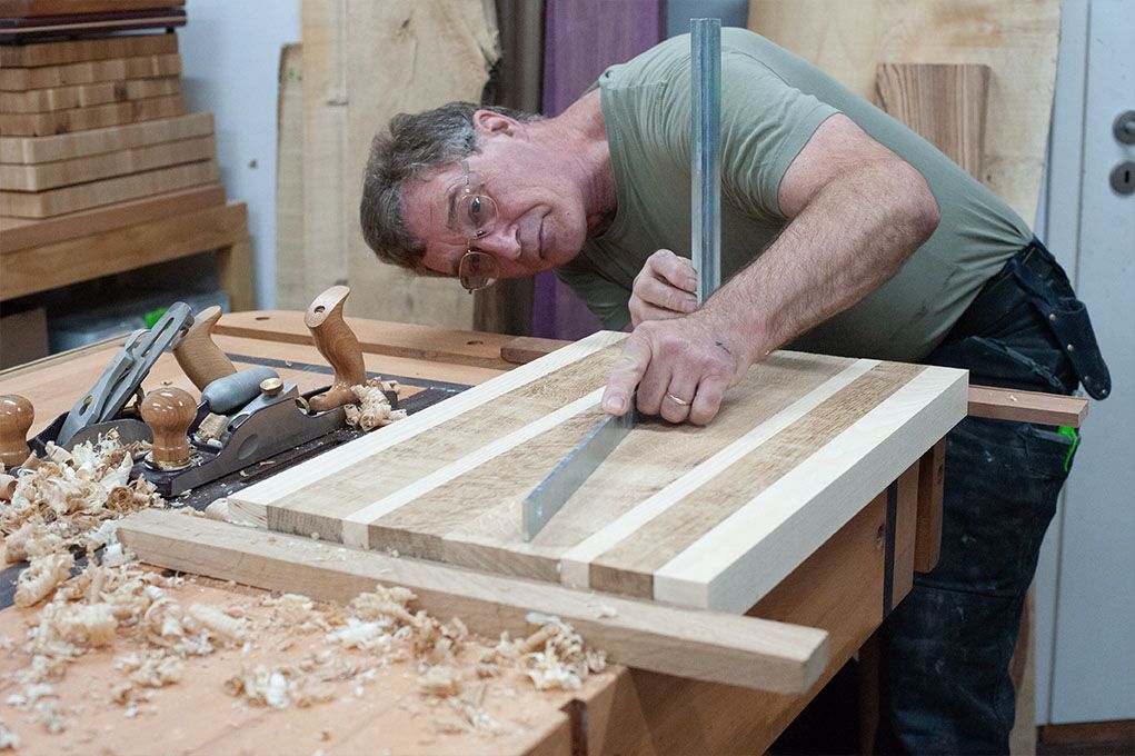 Ein Mann misst ein Stück Holz mit einem Lineal.