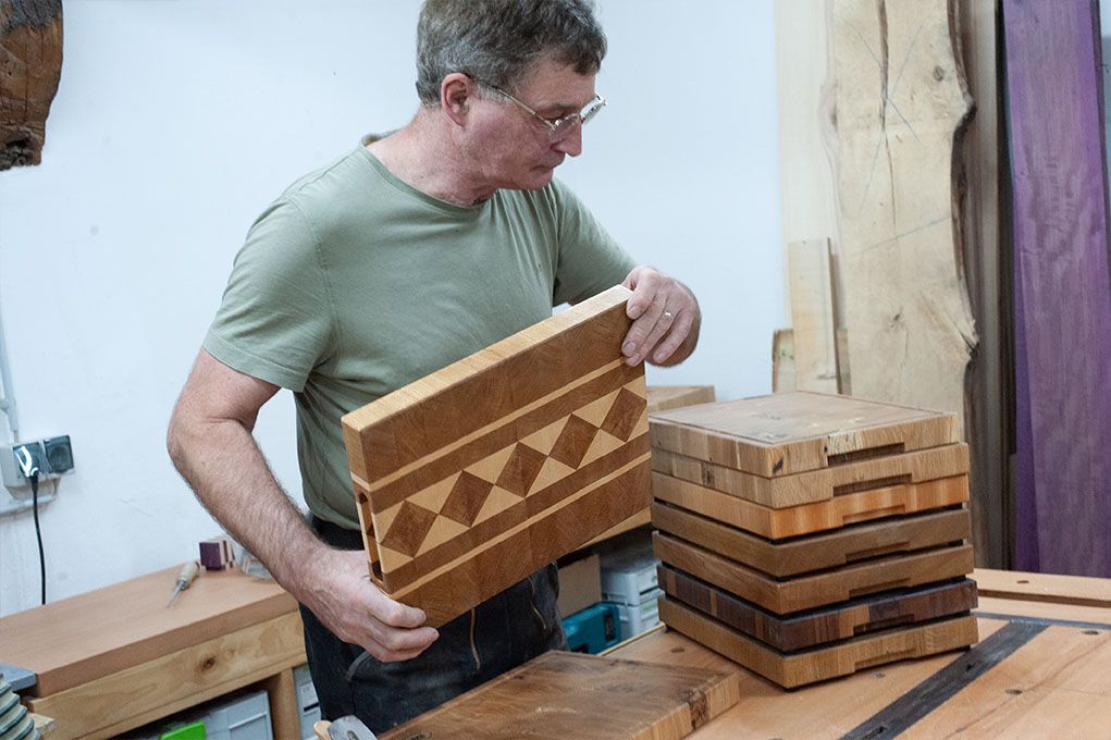 Ein Mann hält ein Holzschneidebrett über einen Stapel Holzschneidebretter.