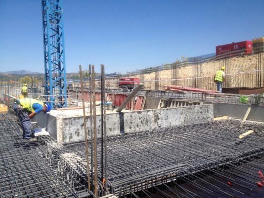 Una obra en construcción con trabajadores y una grúa al fondo.