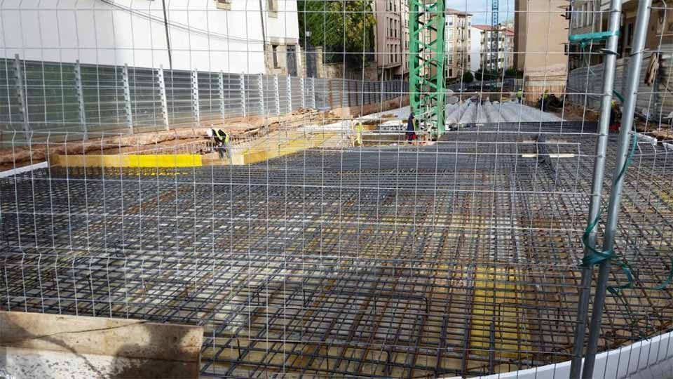 Una obra en construcción con una valla a su alrededor y una grúa al fondo.