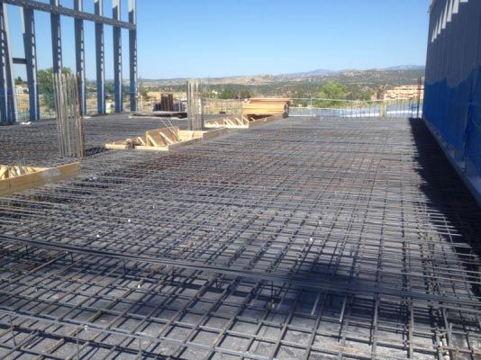 Se está construyendo un piso de concreto con un edificio azul al fondo.