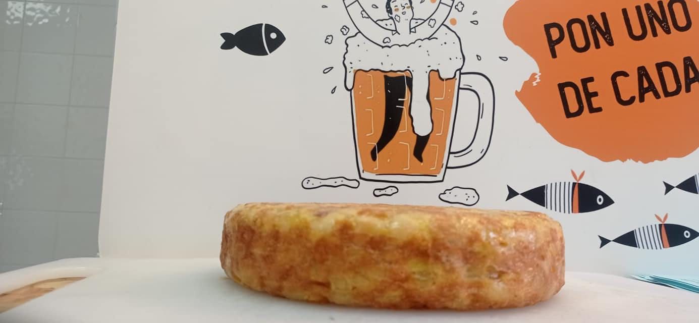 Tortilla española delante de un cartel con una jarra de cerveza e ilustraciones de peces.
