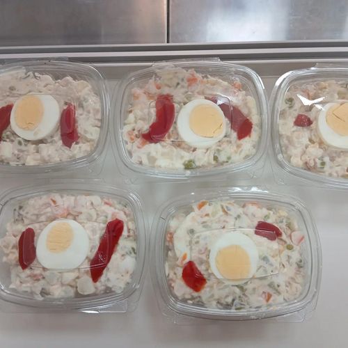 Cinco recipientes de plástico transparente con ensalada de patatas, cubiertos con huevo y pimiento rojo.