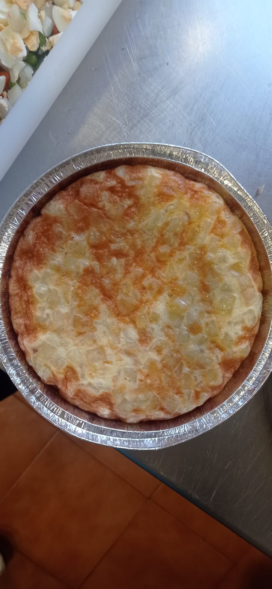 Una tortilla española redonda y de color marrón dorado en un plato recubierto de papel de plata.