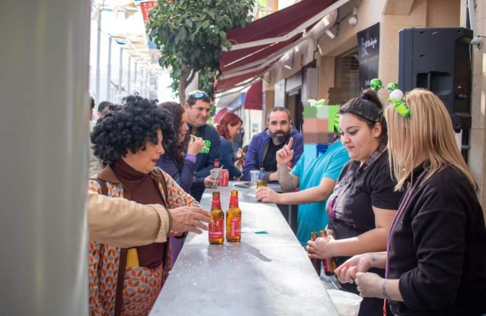 Gente en un bar al aire libre, algunos sirviendo bebidas, con una calle al fondo.