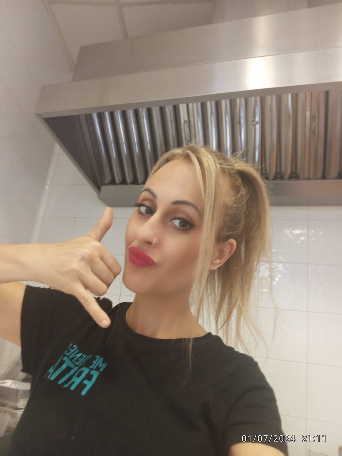 Una mujer rubia con camisa negra hace un gesto con la mano de 