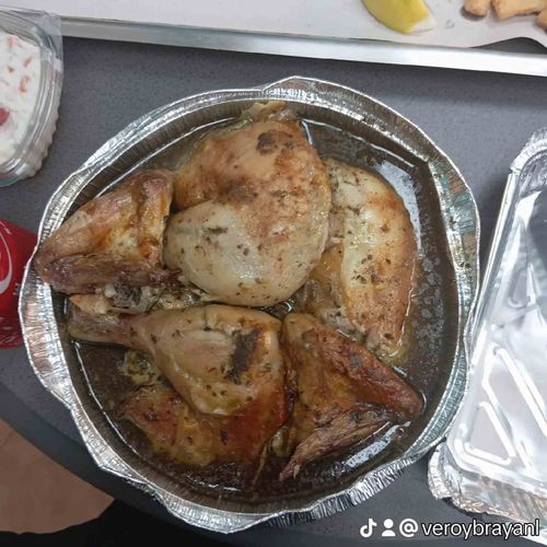 Trozos de pollo asados ​​en un recipiente de aluminio, con un poco de salsa y una bebida.