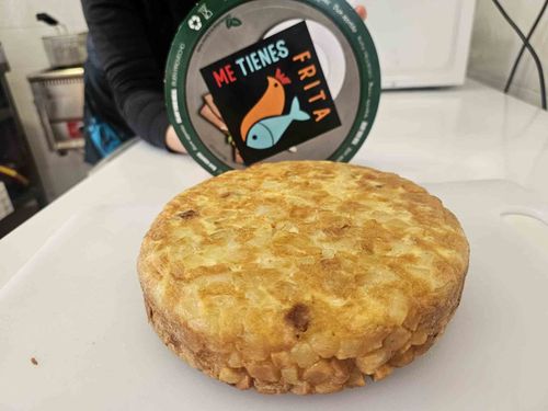 Tortilla española sobre una tabla de cortar con un recipiente que dice 