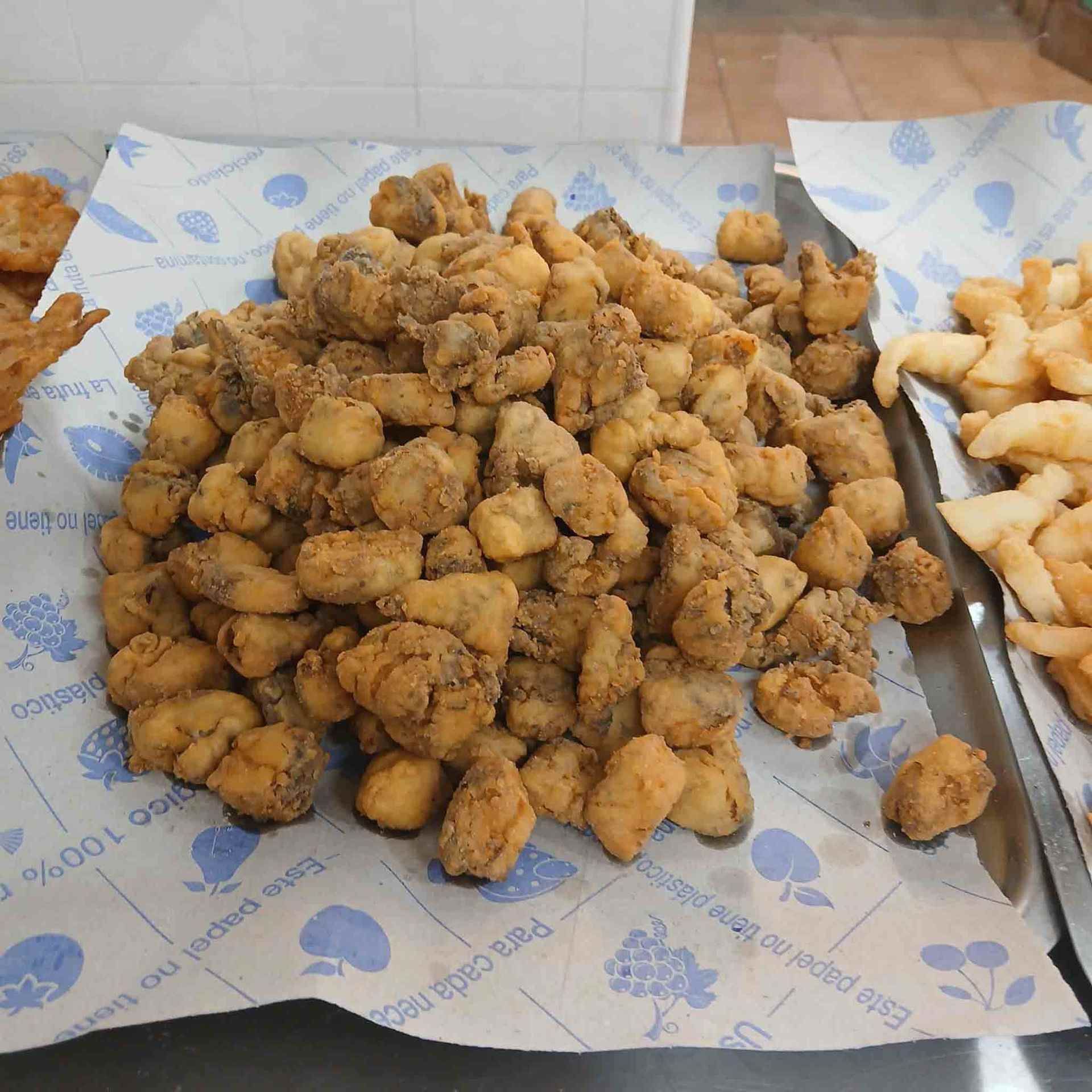Montón de comida frita, posiblemente mariscos, sobre papel estampado en una bandeja de metal.