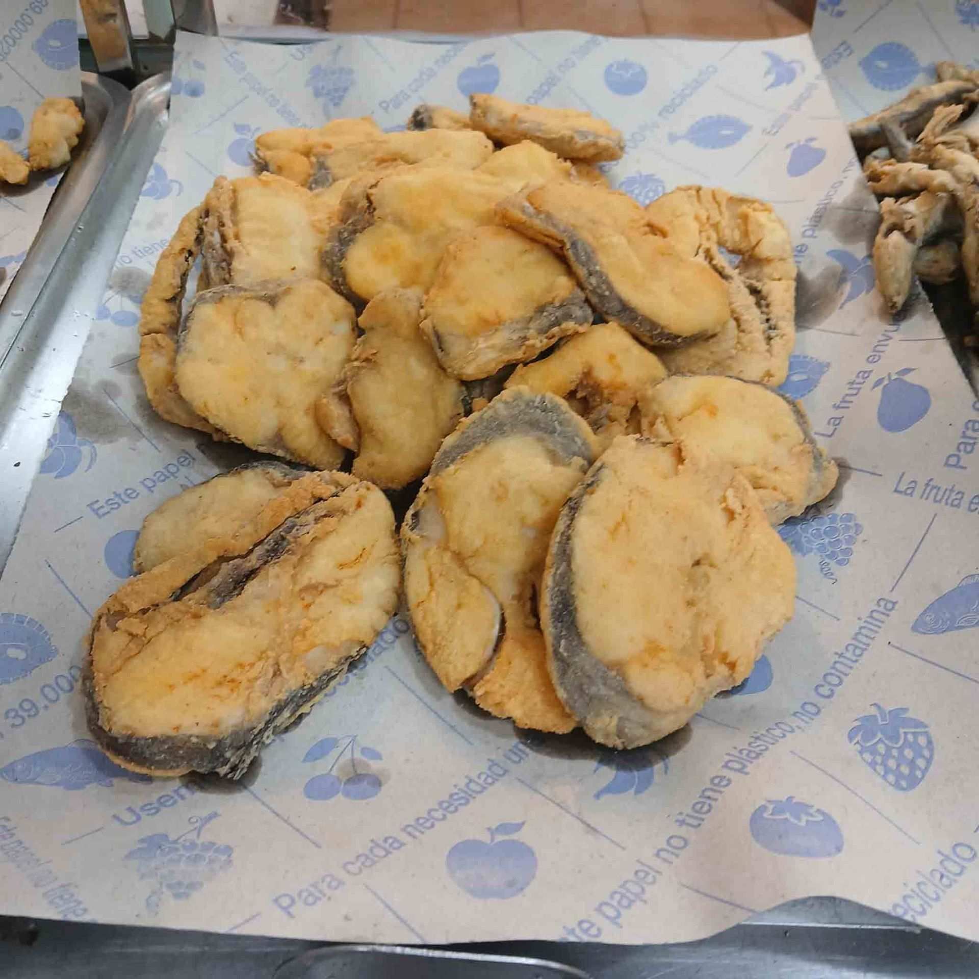 Filetes de pescado fritos dorados sobre papel estampado, probablemente en un restaurante o puesto de comida.