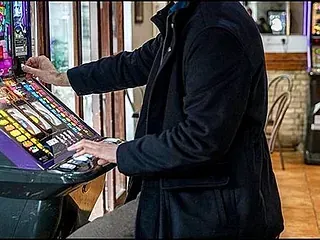 Un hombre con un abrigo negro está jugando a una máquina tragamonedas.