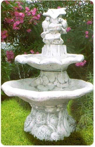 Una fuente blanca en un jardín con flores al fondo.