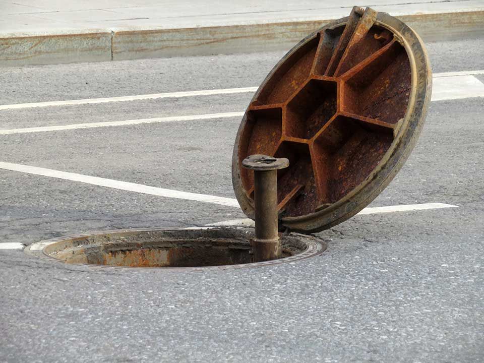 Plaque d'égout ouverte avec un couvercle hexagonal rouillé sur une route pavée.