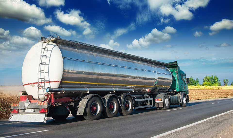 Camion-citerne sur une route sous un ciel bleu, transportant une cargaison liquide.