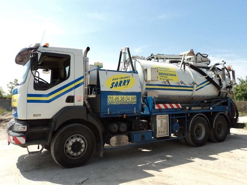 Camion aspirateur blanc et bleu avec une cuve cylindrique, stationné par une journée ensoleillée.