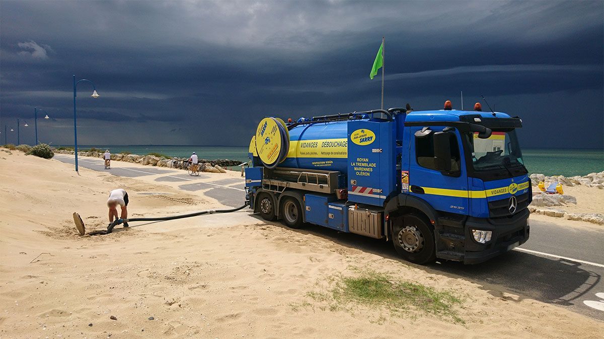 Camion de ramassage bleu sur la plage, sous un ciel couvert de sombres nuages ​​d'orage.