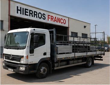 Camión blanco de plataforma estacionado frente a un edificio con letrero de “Hierros Franco”.