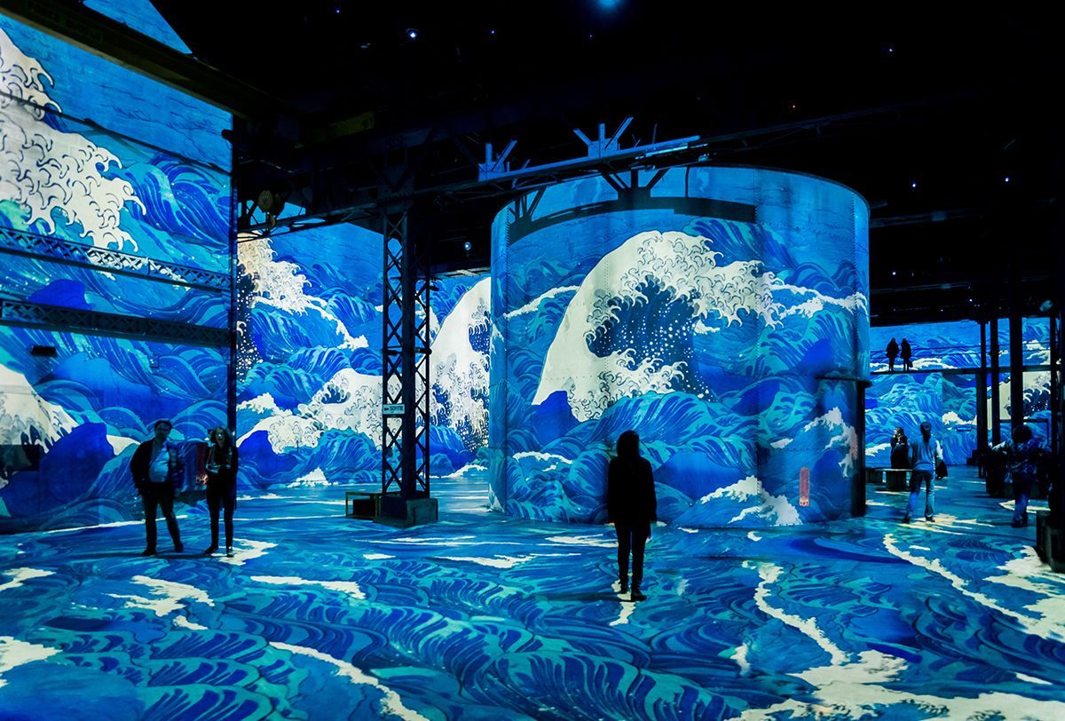 Installation featuring blue wave projections on walls and floor; people walking.