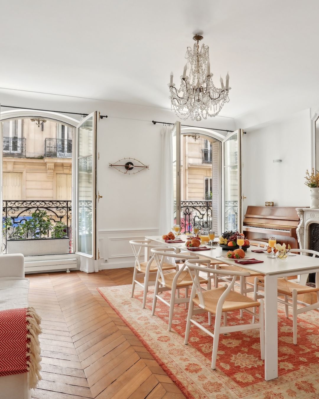 Dining room with white table, chairs, chandelier, and open balcony doors overlooking a Parisian street.