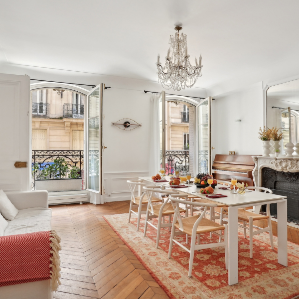 Elegant dining room with white table and chairs, chandelier, and open balcony doors.