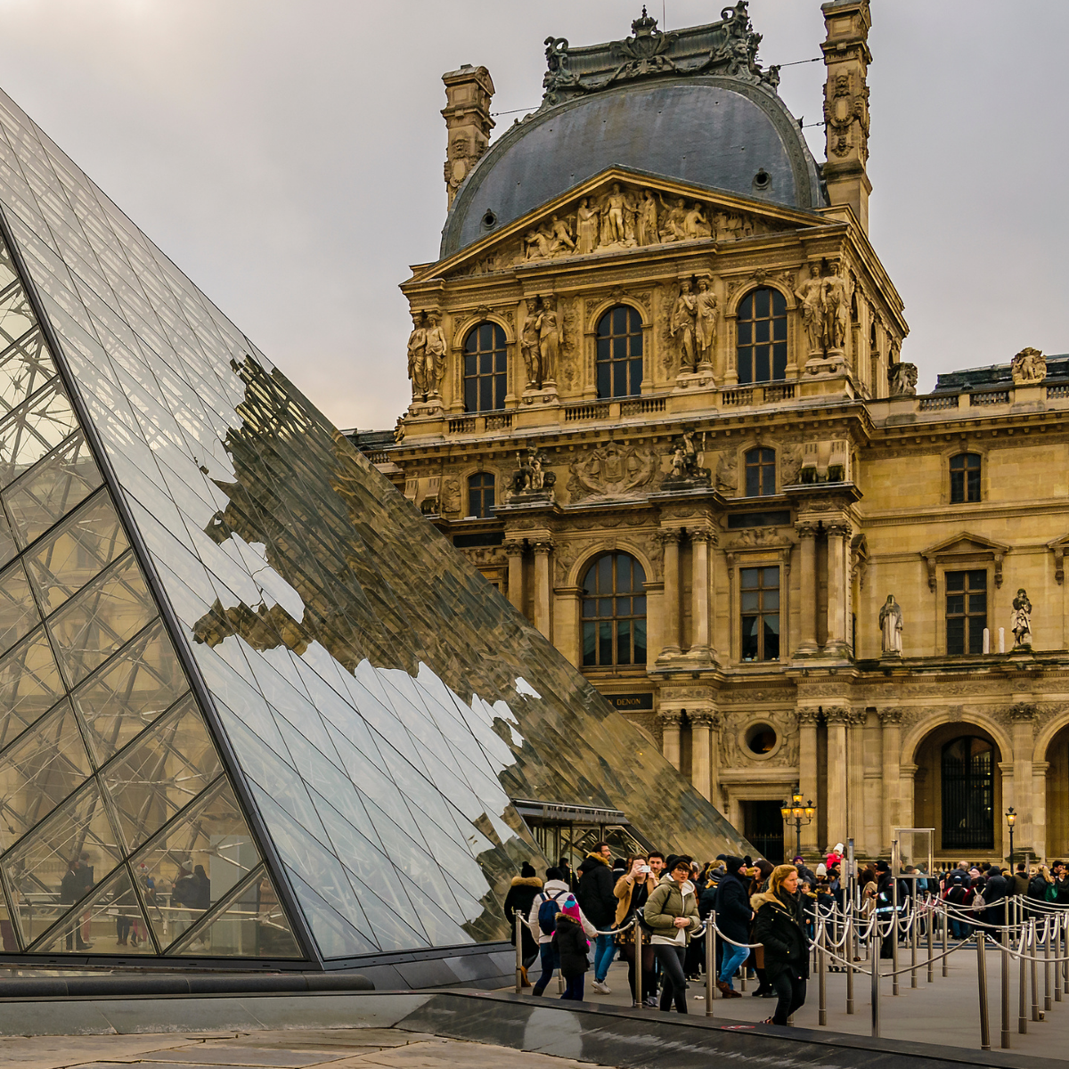 Narrow Parisian street lined with tall, cream-colored buildings. Street slopes downward; pedestrians and shops visible. 