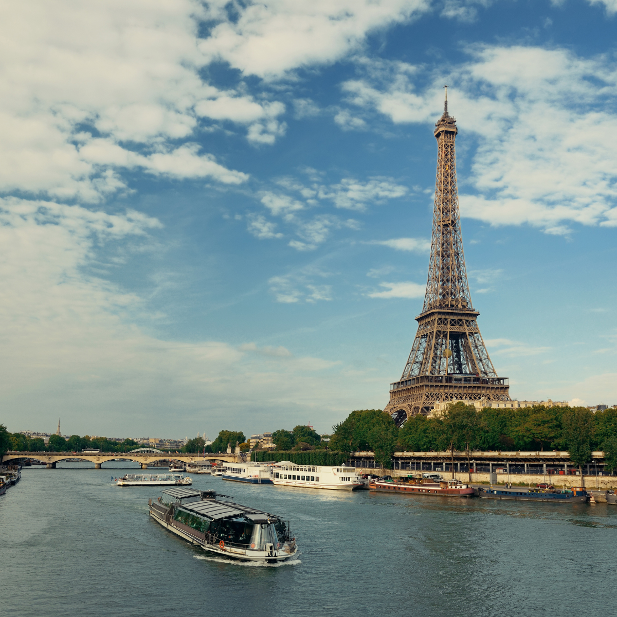 Narrow Parisian street lined with tall, cream-colored buildings. Street slopes downward; pedestrians and shops visible. 