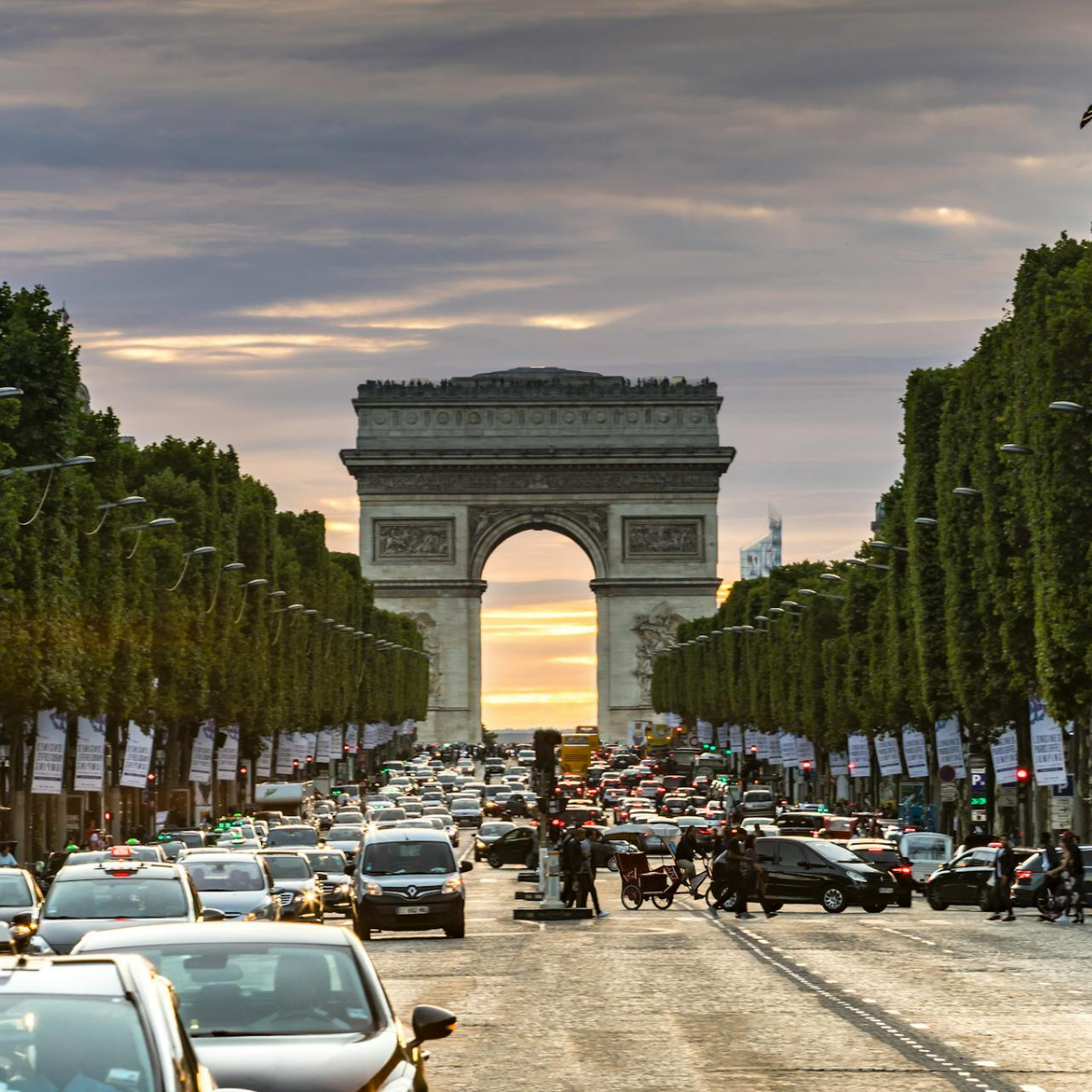 Narrow Parisian street lined with tall, cream-colored buildings. Street slopes downward; pedestrians and shops visible. 