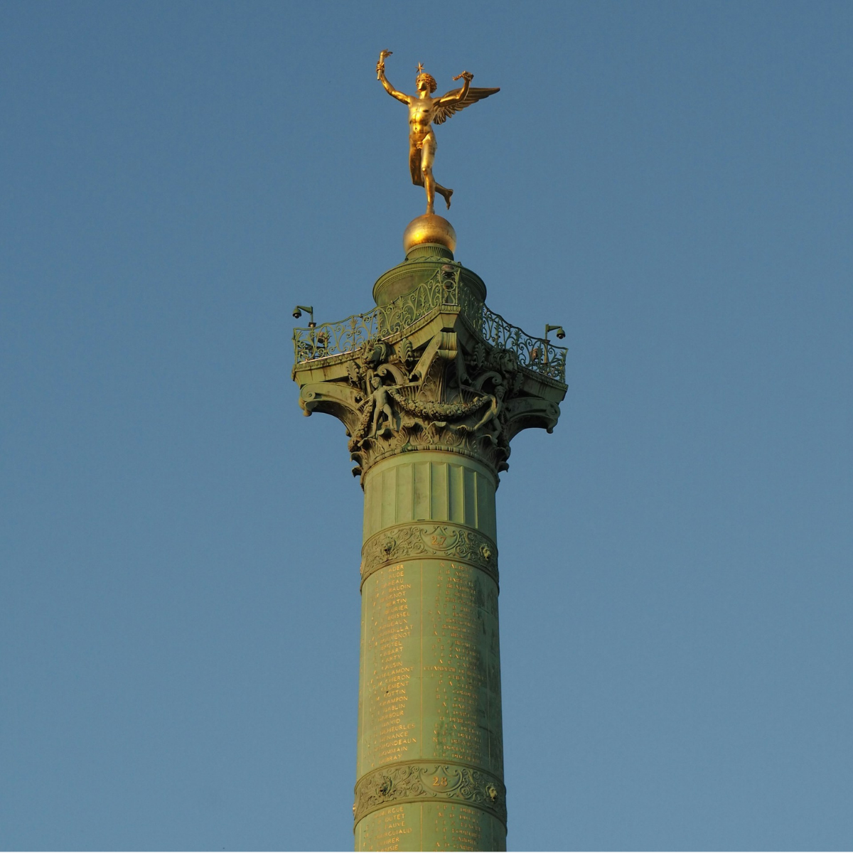 Narrow Parisian street lined with tall, cream-colored buildings. Street slopes downward; pedestrians and shops visible.