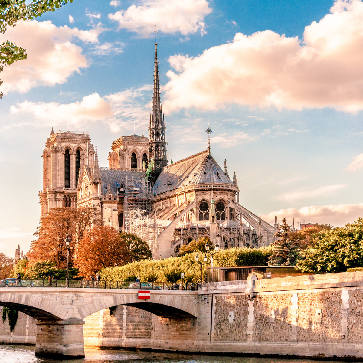 Narrow Parisian street lined with tall, cream-colored buildings. Street slopes downward; pedestrians and shops visible. 