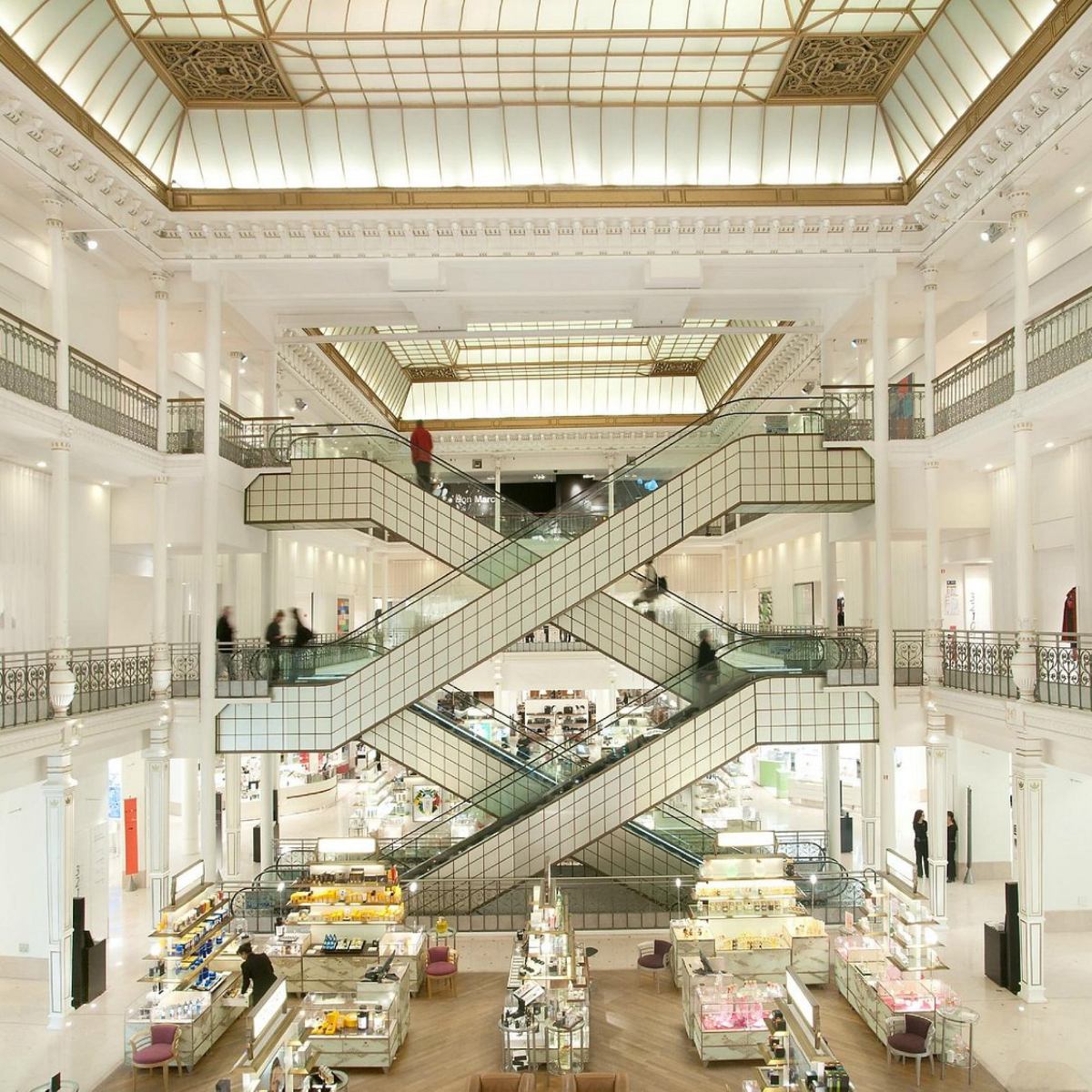 Narrow Parisian street lined with tall, cream-colored buildings. Street slopes downward; pedestrians and shops visible. 
