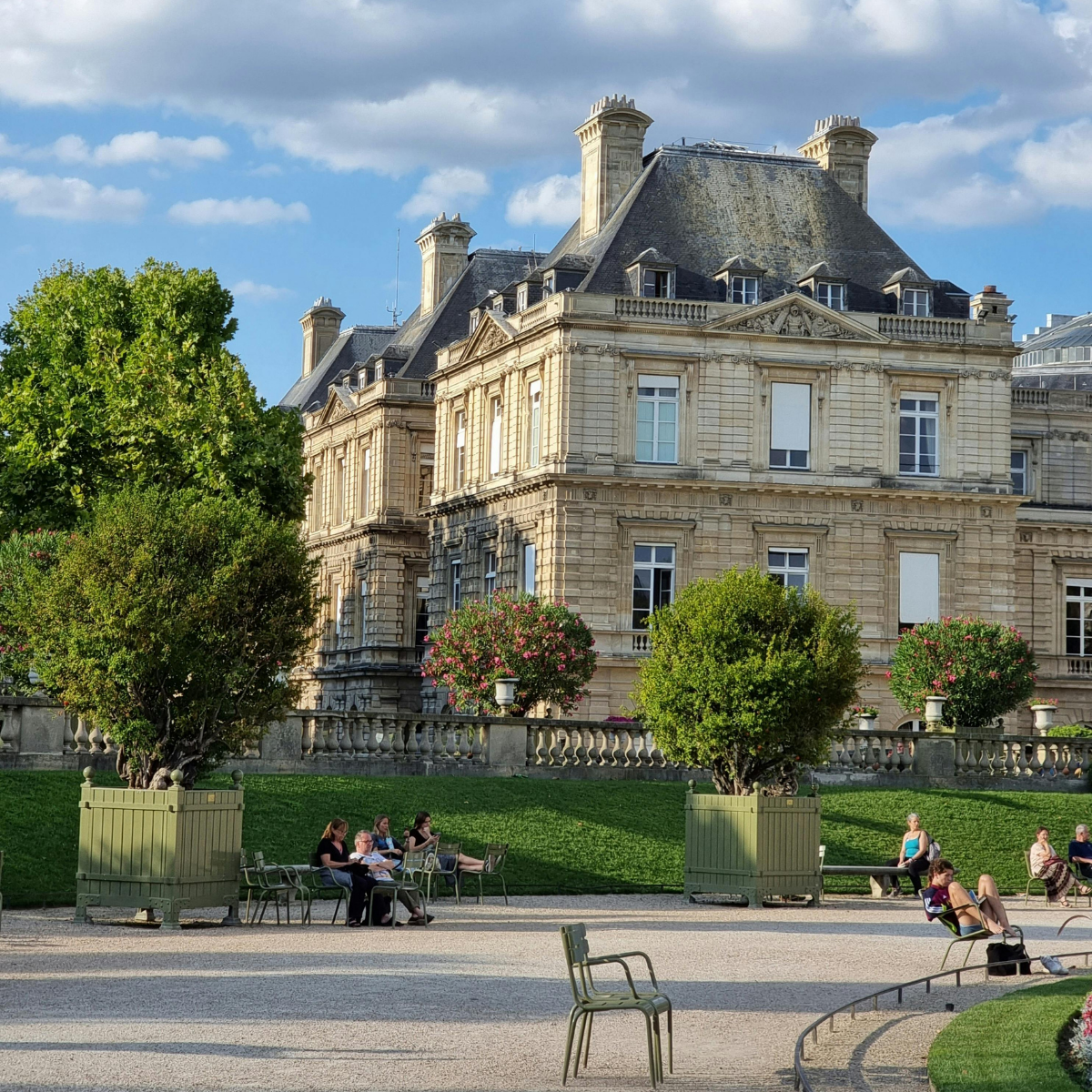 Narrow Parisian street lined with tall, cream-colored buildings. Street slopes downward; pedestrians and shops visible. 