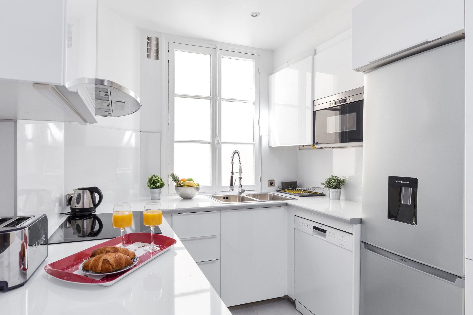 White kitchen with built-in appliances and a window over the sink. A tray with breakfast sits on the countertop.