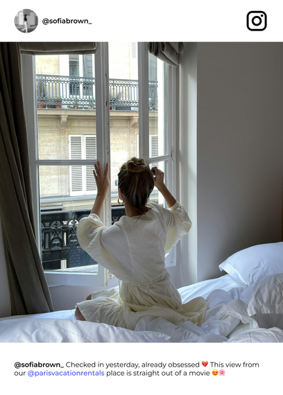 Woman in robe by a window, Paris building view. Hands raised, morning light.