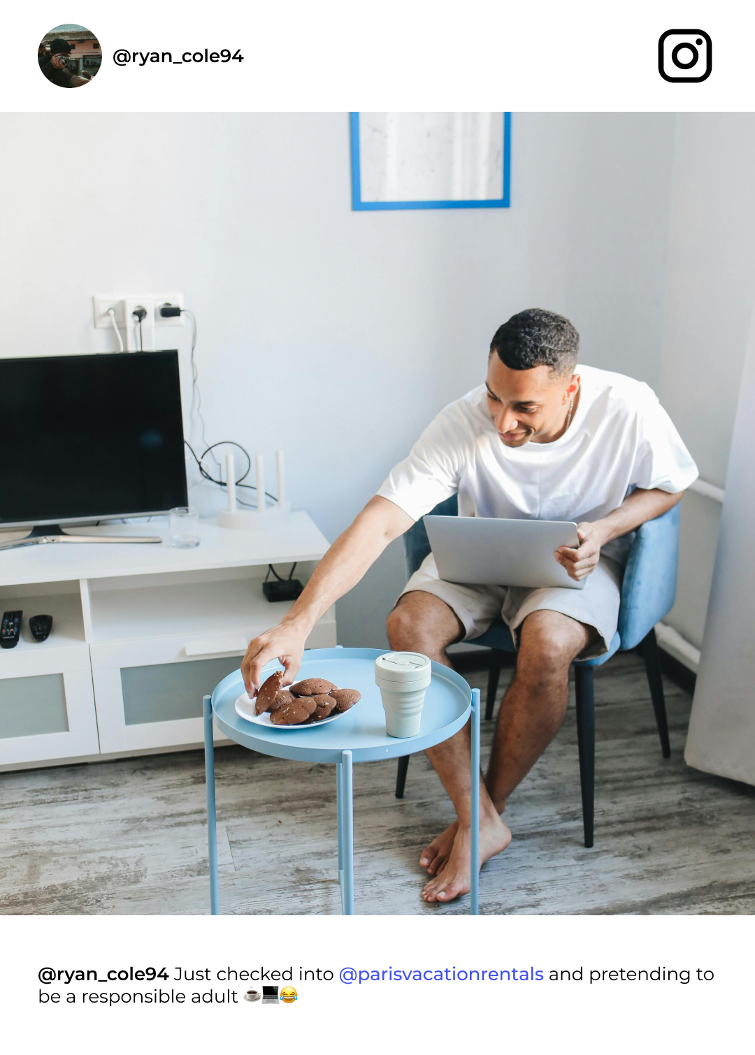Man seated, working on laptop, reaching for pastry on table with coffee. Interior.