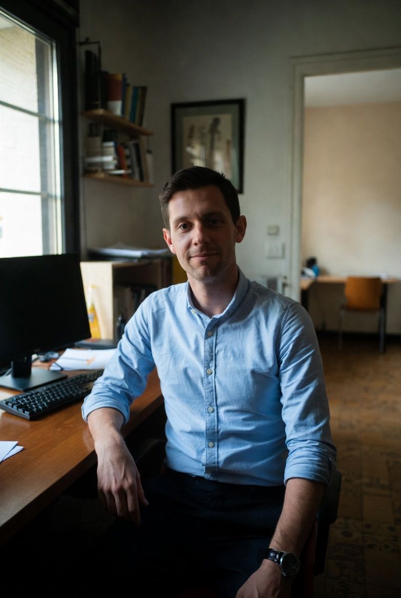 Man with glasses and helmet smiling, carrying greyhound dog in backpack on city street.