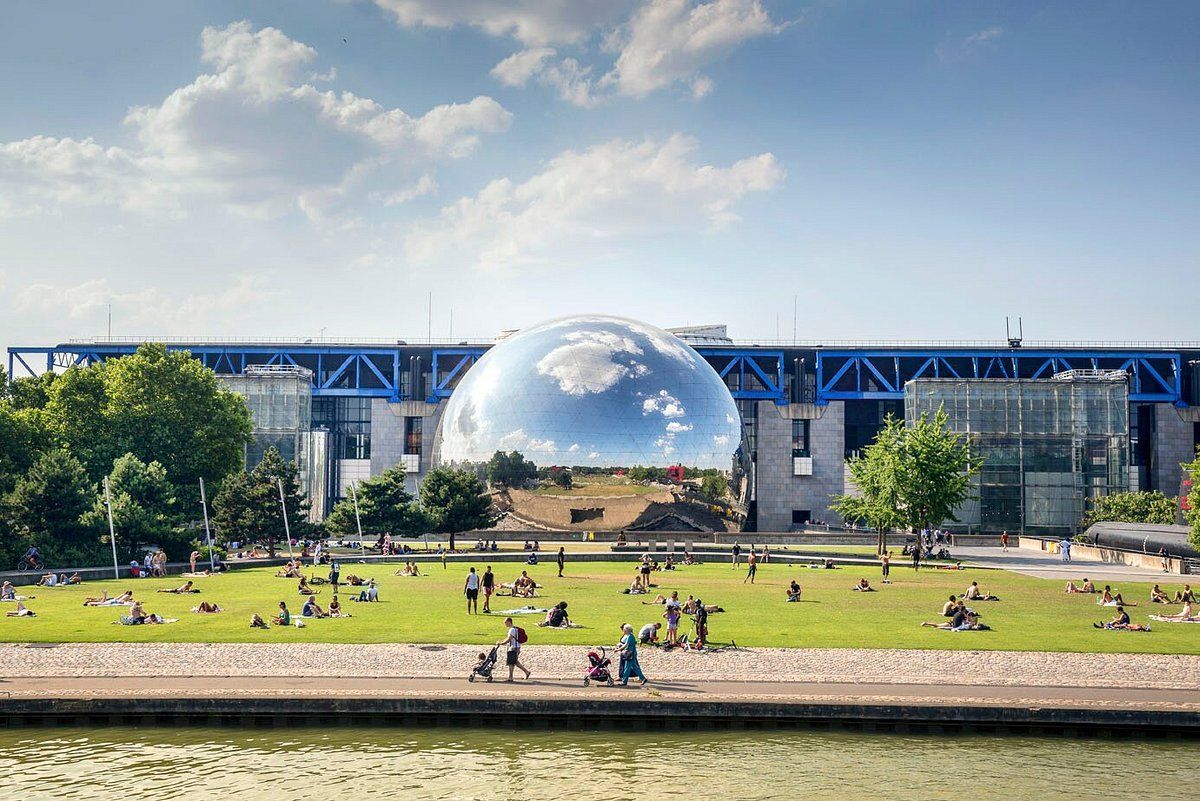 A large reflective sphere in a park, part of a building complex. People are relaxing on the lawn in front.