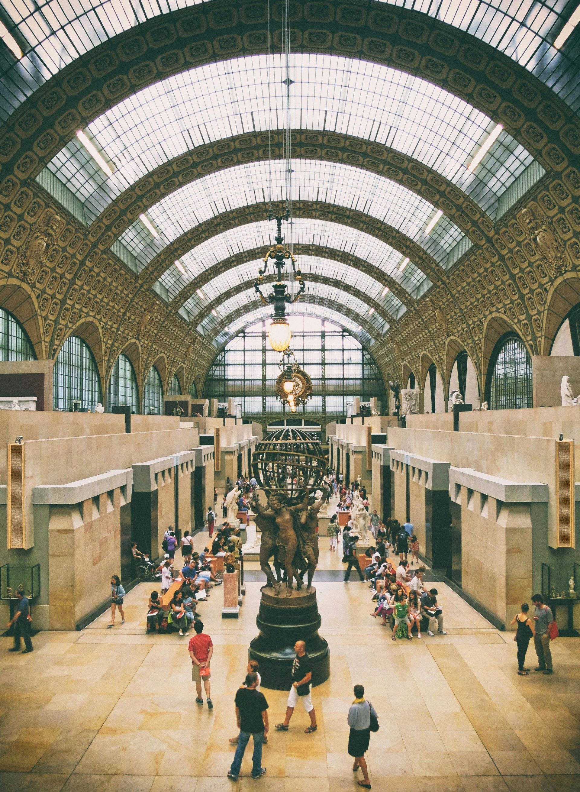 Interior view of the Musée d'Orsay, Paris. A grand hall with a high arched ceiling, visitors are milling about.