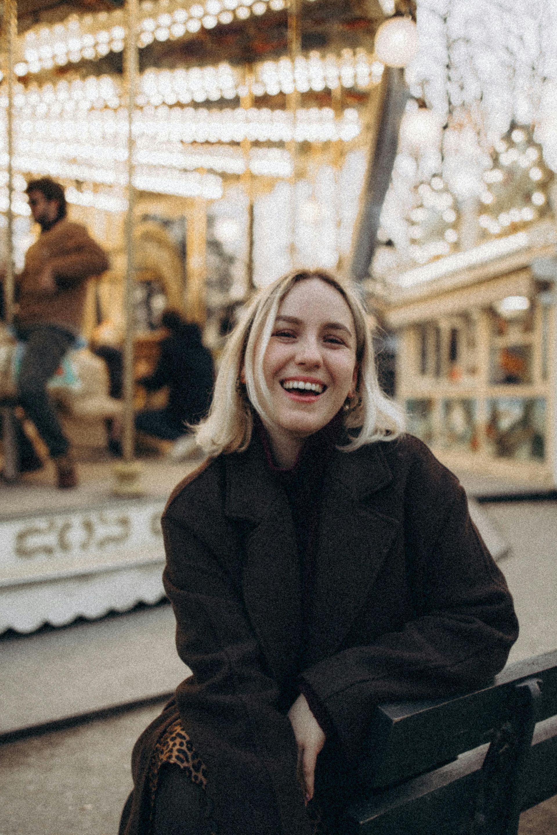 A woman is sitting on a bench in front of a merry go round.
