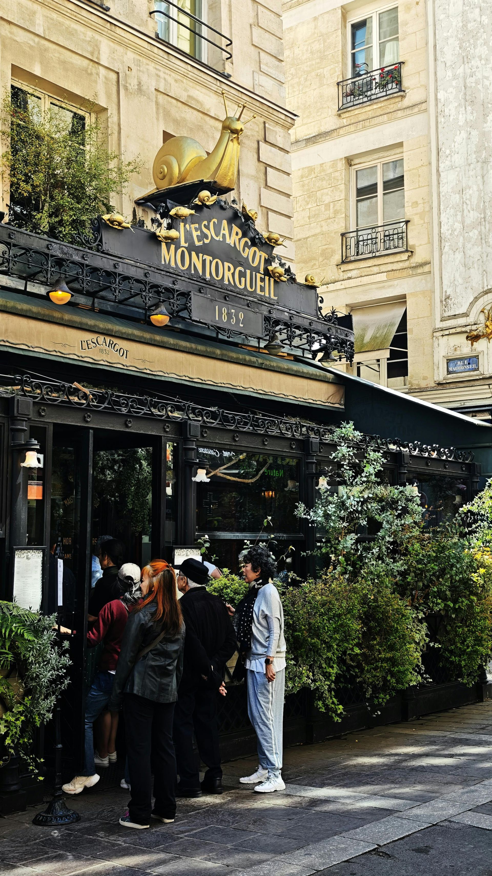 People queue outside a restaurant in Paris, France, under a black awning and sign that reads