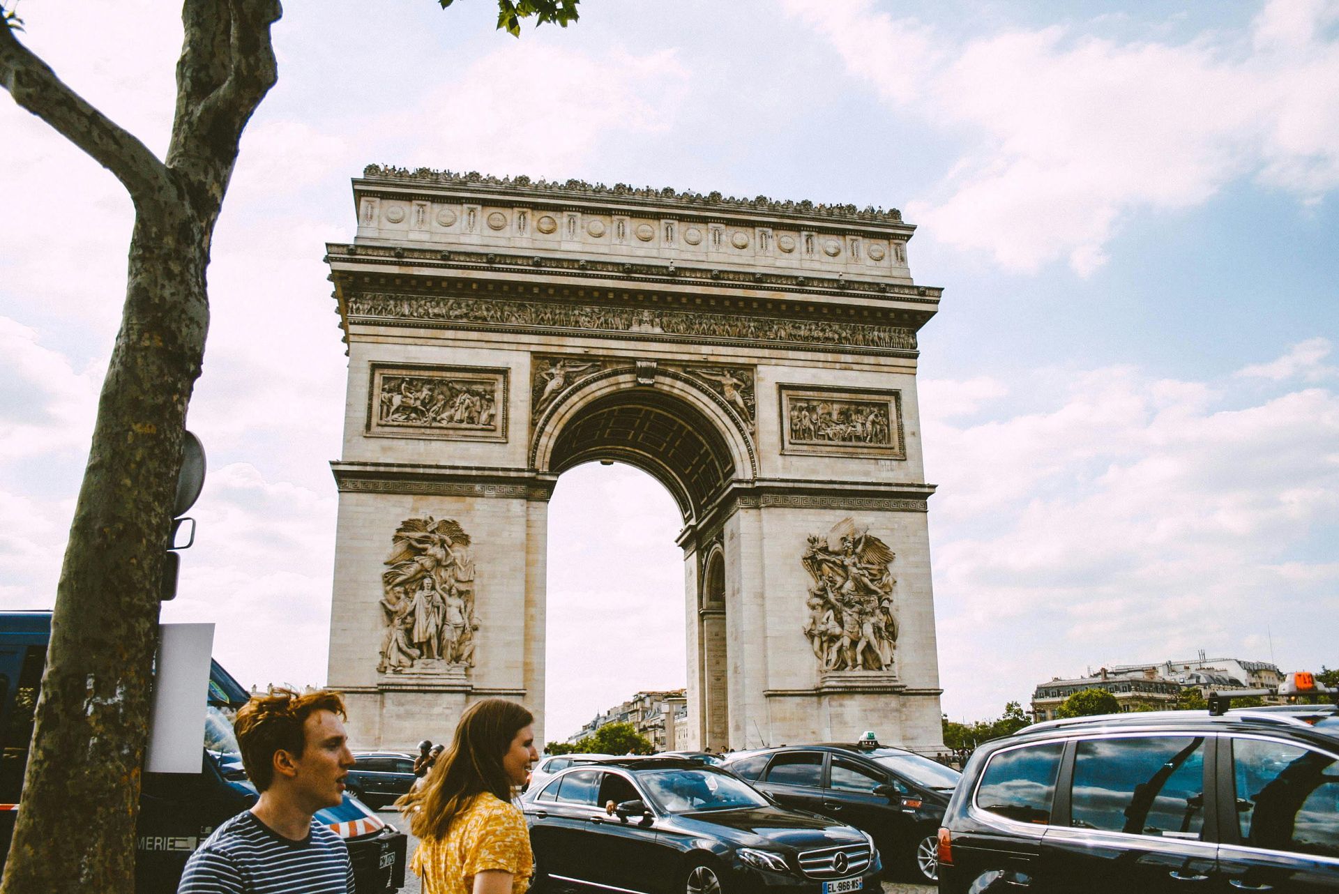 Arc de Triomphe in Paris, France, with cars and people in front of it on a sunny day.