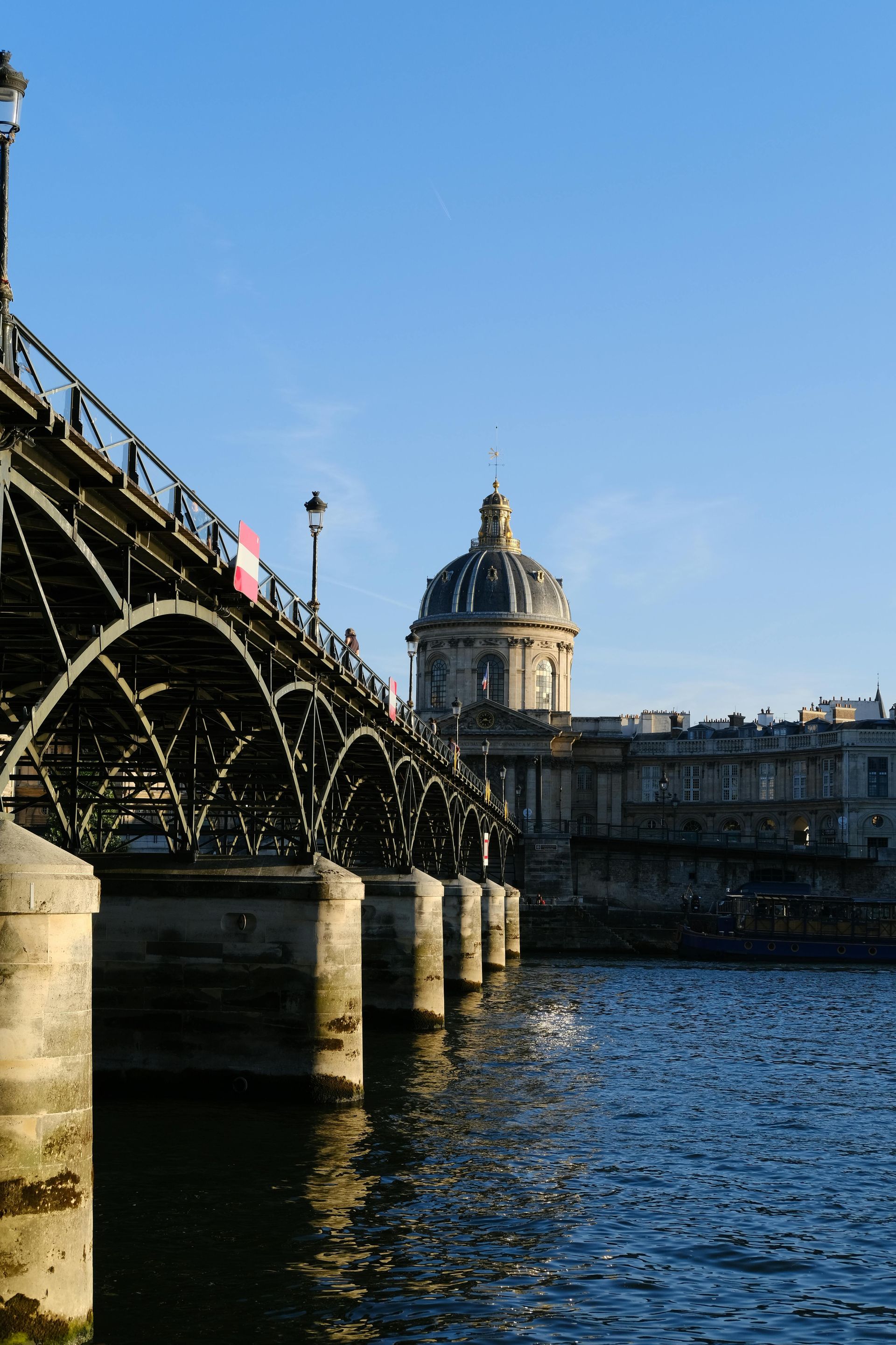 Bridge over water with a domed building and blue sky in the background.