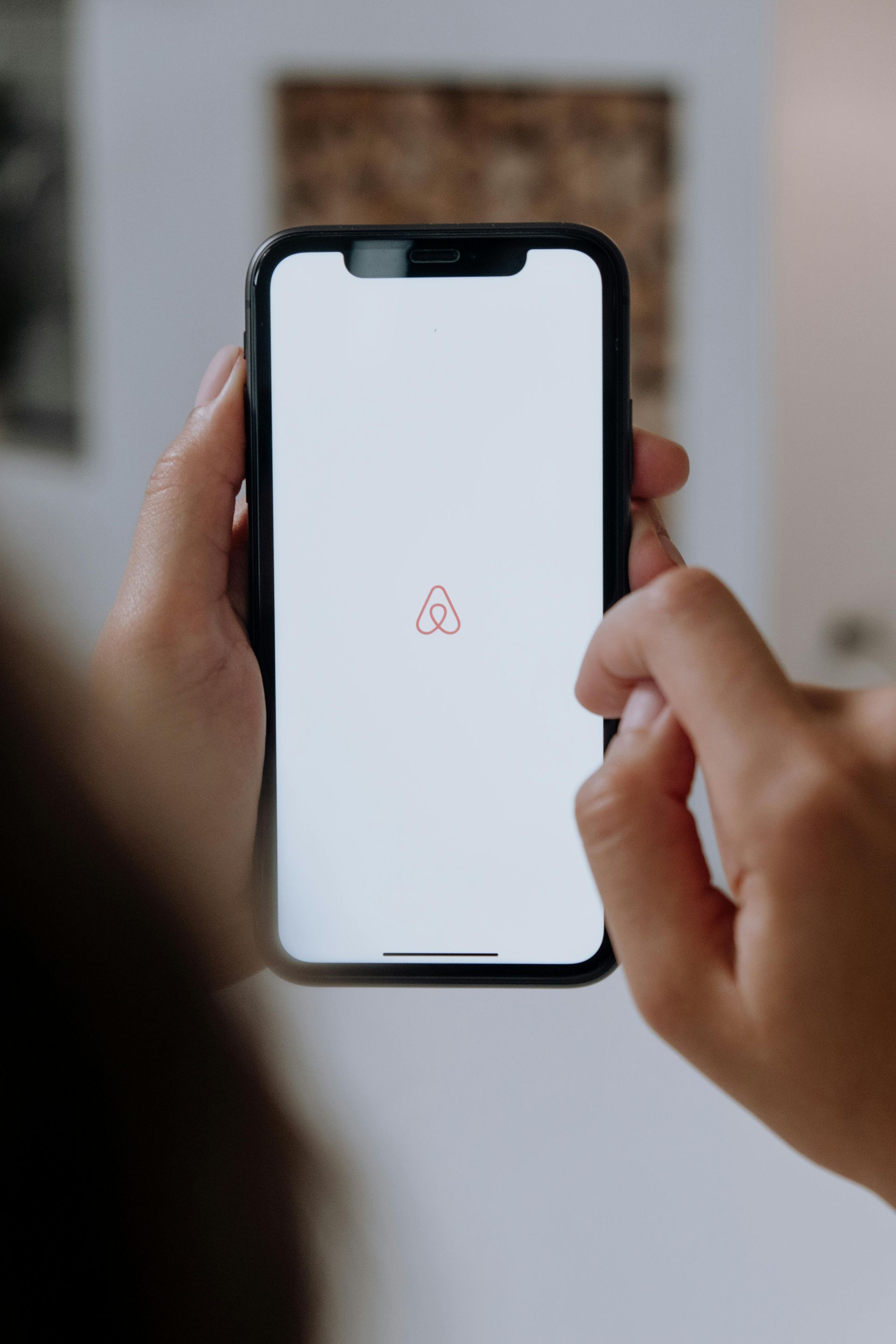 Person holding a black smartphone displaying the Airbnb logo on a white screen.